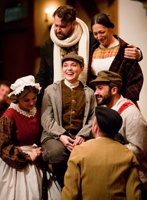 The Cratchit family, all in Victorian middle class clothes, gather around Tiny Tim sitting in the middle. Martha kneels to Tim's right, the brothers are kneeling to his left, and Bob Cratchit has his arm around Mrs. Cratchit standing behin Tim.
